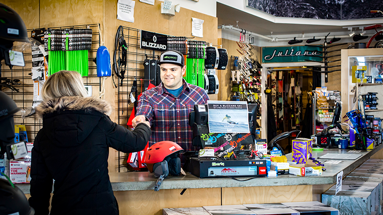 Woman handing cashier debit card to make purchase at bike and snow shop