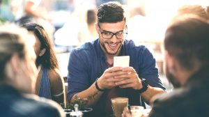 Man using Zelle on Smartphone sitting with friends