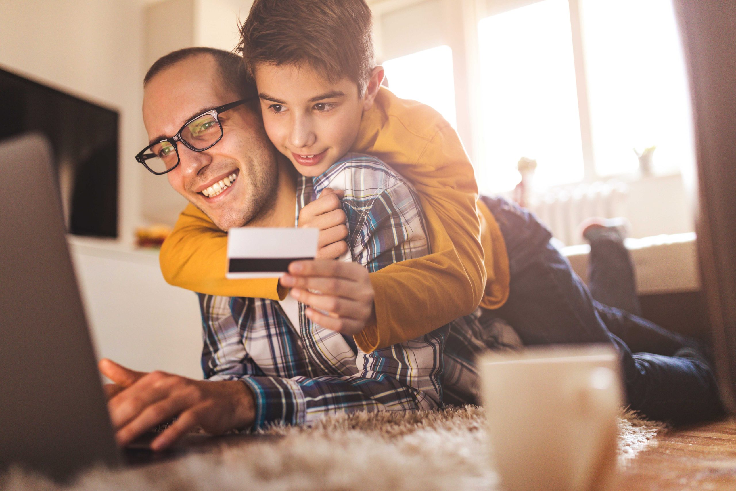 Father and son looking at a computer together while holding a debit card