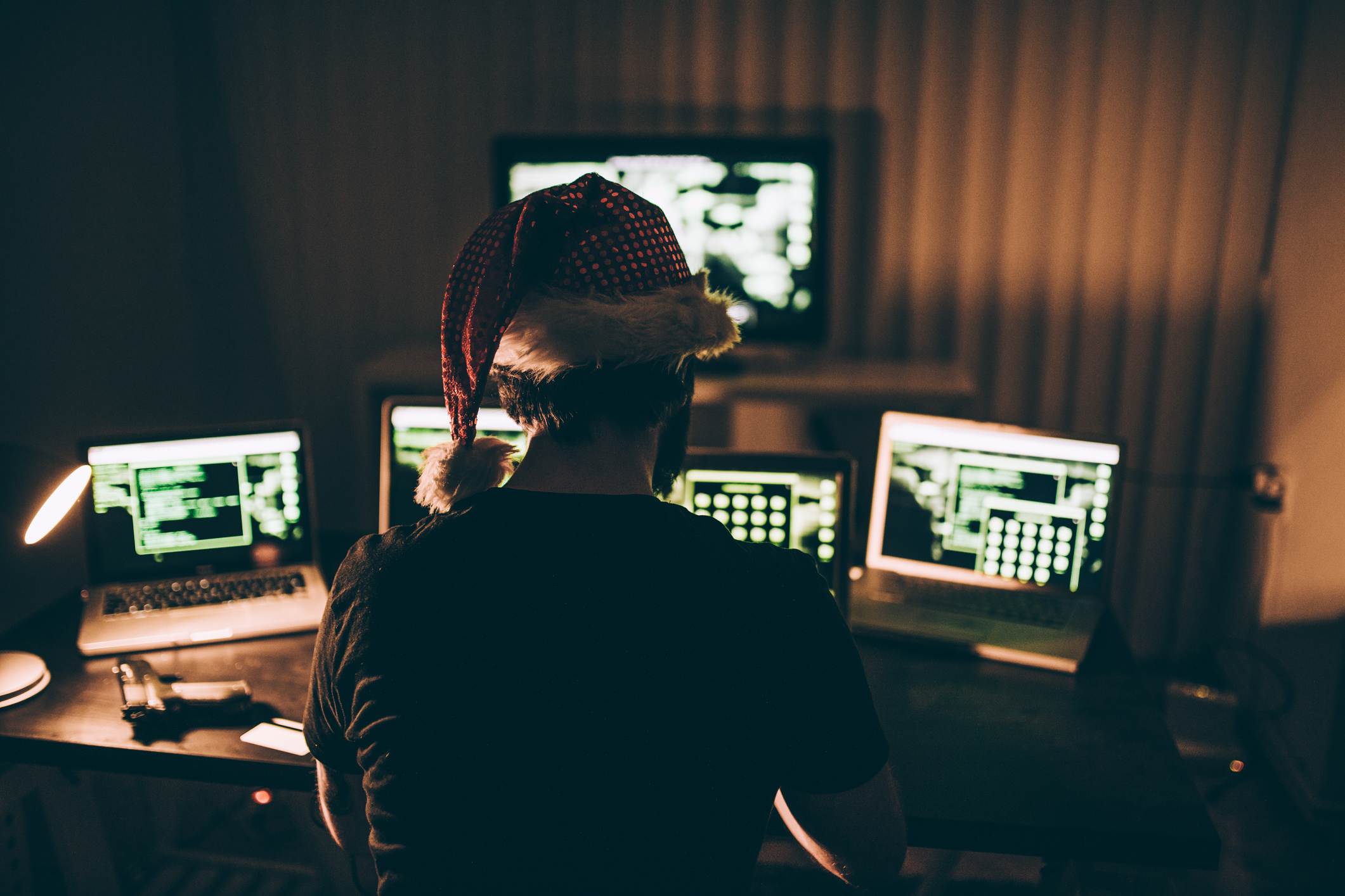 cybercriminal sitting in a dark room with holiday hat on looking at multiple computer screens